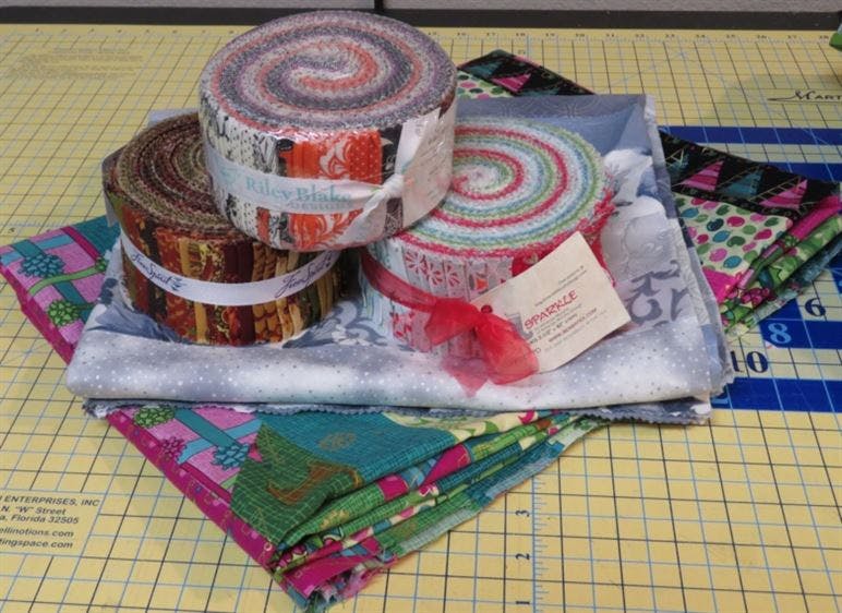 Three jelly rolls placed on top of two jelly roll race quilts that have been folded up.